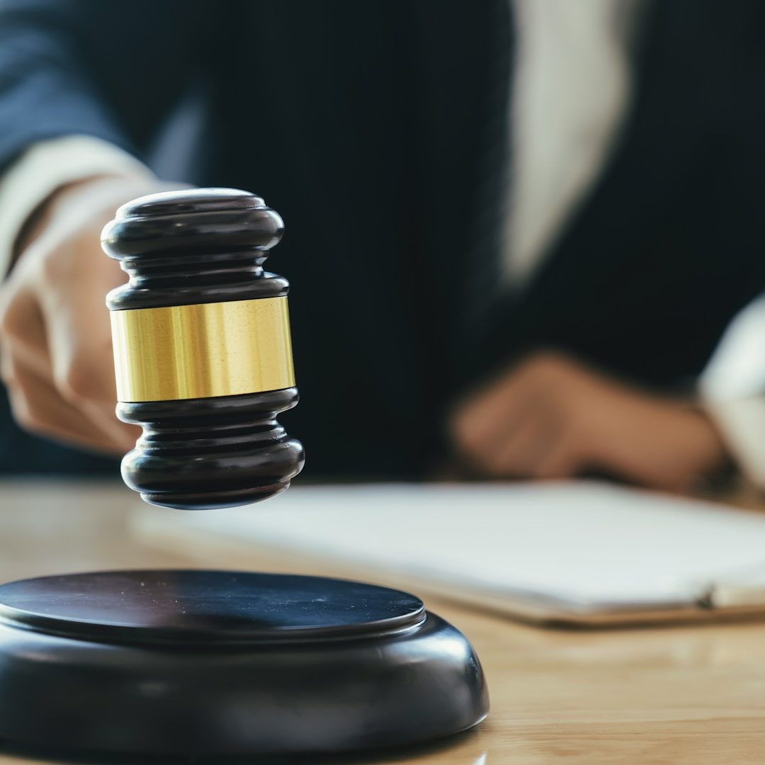 Richter schlägt mit einem Hammer auf einen Richterstuhl vor einem Notizblock.