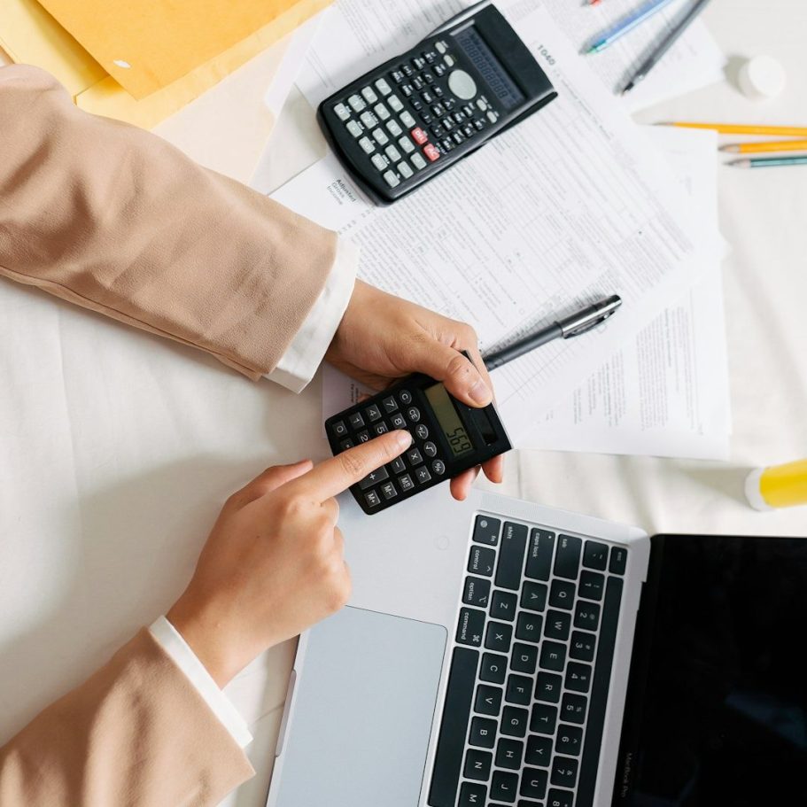 Beleihungswertermittlung Hände arbeiten an einem Taschenrechner und Laptop, umgeben von Notizen und Stiften.