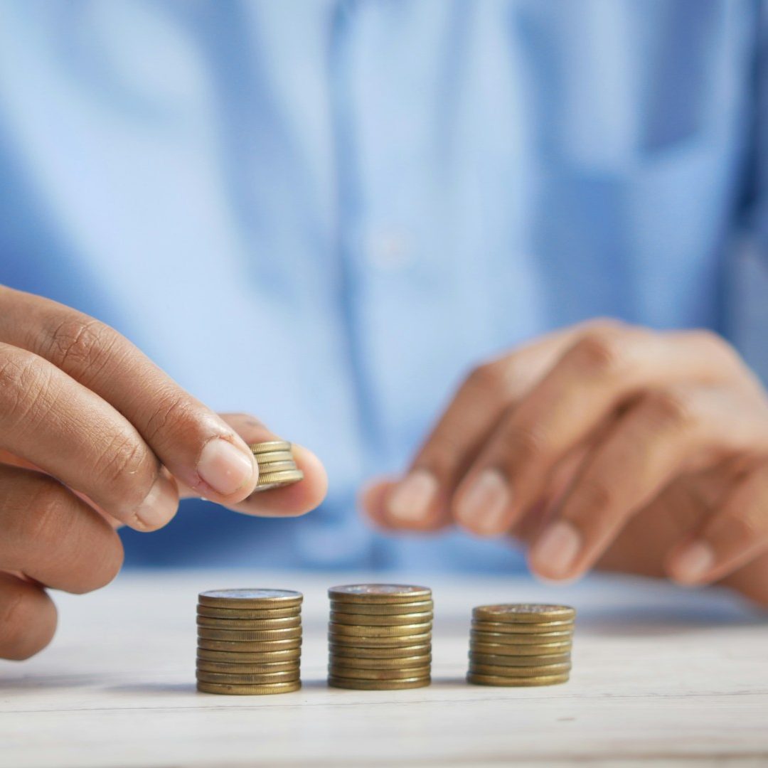 Eine Hand legt eine Münze auf einen Stapel von Münzen auf einem Tisch.